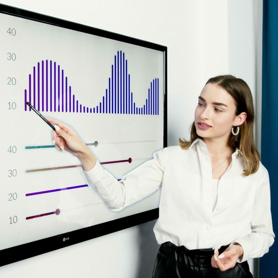 Businesswoman presenting data on a large digital screen in a modern office setting.